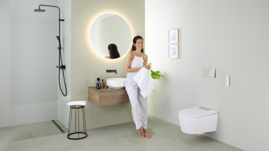 Donna appoggiata sul lavabo in un bagno con WC doccia Geberit AquaClean Sela e lavabo e mobili Geberit VariForm
