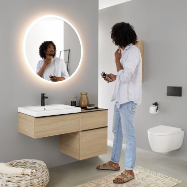 Uomo che si guarda in uno specchio rotondo con luce Geberit Option Uomo che si guarda in uno specchio rotondo con luce Geberit Option