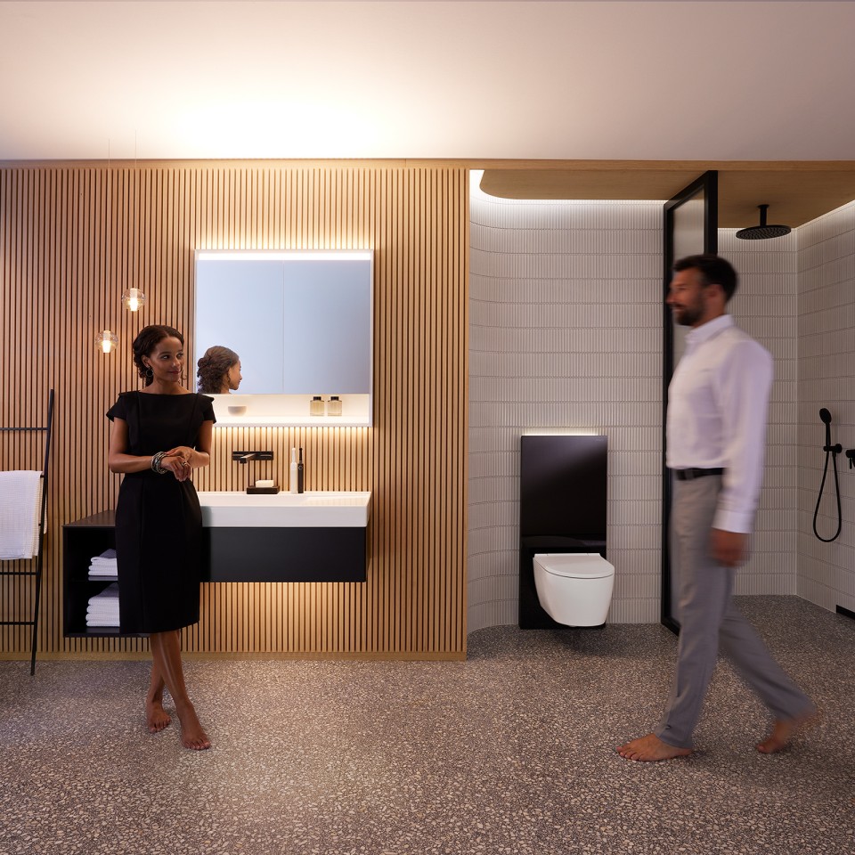 Uomo e donna in un bagno perfettamente illuminato con mobili da bagno e ceramiche Geberit ONE (© Geberit)
