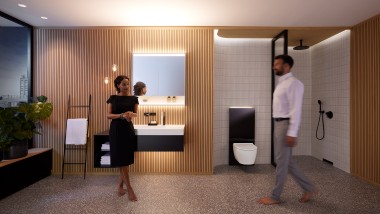 Uomo e donna in un bagno perfettamente illuminato con mobili da bagno e ceramiche Geberit ONE (© Geberit)