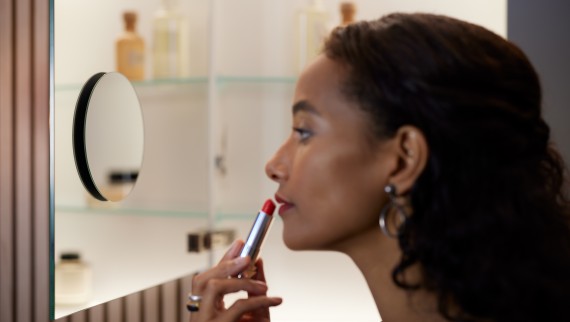 Donna che applica il rossetto davanti a uno specchio ingranditore (© Geberit)