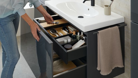 Donna che prende un pennello da un mobile lavabo Geberit Acanto con finitura lava Donna che prende un pennello da un mobile lavabo Geberit Acanto con finitura lava