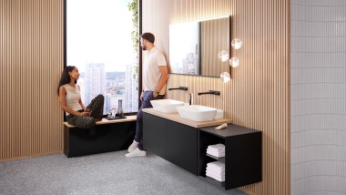 Donna seduta sul davanzale di un bagno arredato con prodotti Geberit ONE, mentre parla con un uomo Donna seduta sul davanzale di un bagno arredato con prodotti Geberit ONE, mentre parla con un uomo