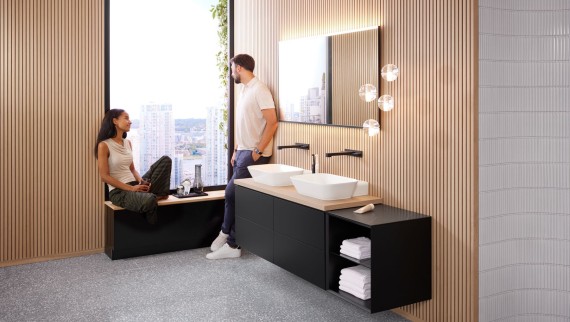 Una donna e un uomo in un ampio bagno con lavabo doppio Geberit ONE, specchio Option Una donna e un uomo in un ampio bagno con lavabo doppio Geberit ONE, specchio Option
