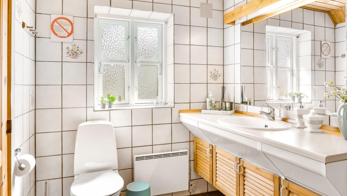 Bagno originale con vaso WC a pavimento, piastrelle bianche e mobili in legno (© @triner2 and @strandparken3)