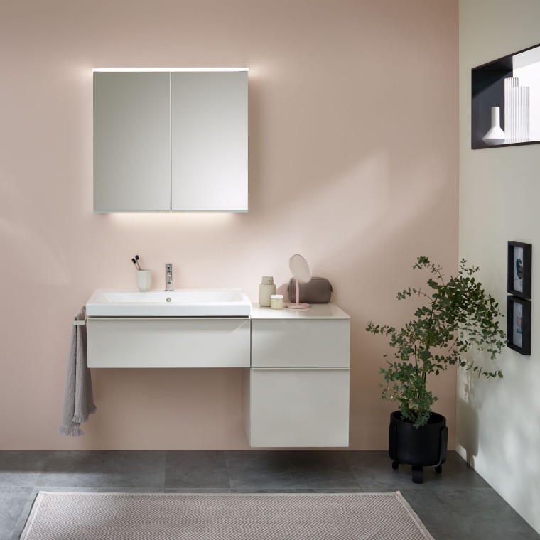 Zona lavabo con mobili da bagno, lavabo e mobile specchio di Geberit davanti a una parete color pastello Zona lavabo con mobili da bagno, lavabo e mobile specchio di Geberit davanti a una parete color pastello