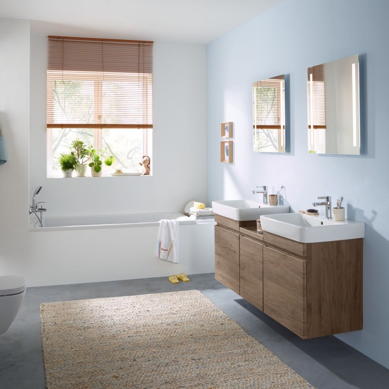 Bagno per famiglia con parete azzurra e mobili da bagno in legno di noce, mobile specchio, placca di comando e sanitari in ceramica di Geberit Bagno per famiglia con parete azzurra e mobili da bagno in legno di noce, mobile specchio, placca di comando e sanitari in ceramica di Geberit
