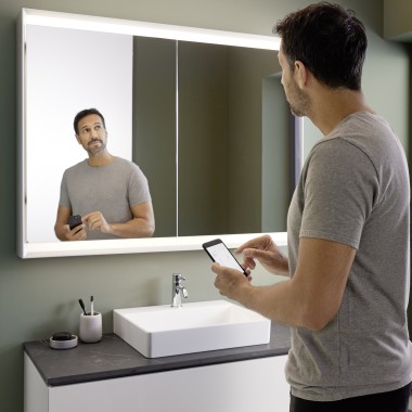 L'uomo controlla l'illuminazione dell'armadietto a specchio Geberit ONE con il suo smartphone (© Geberit)