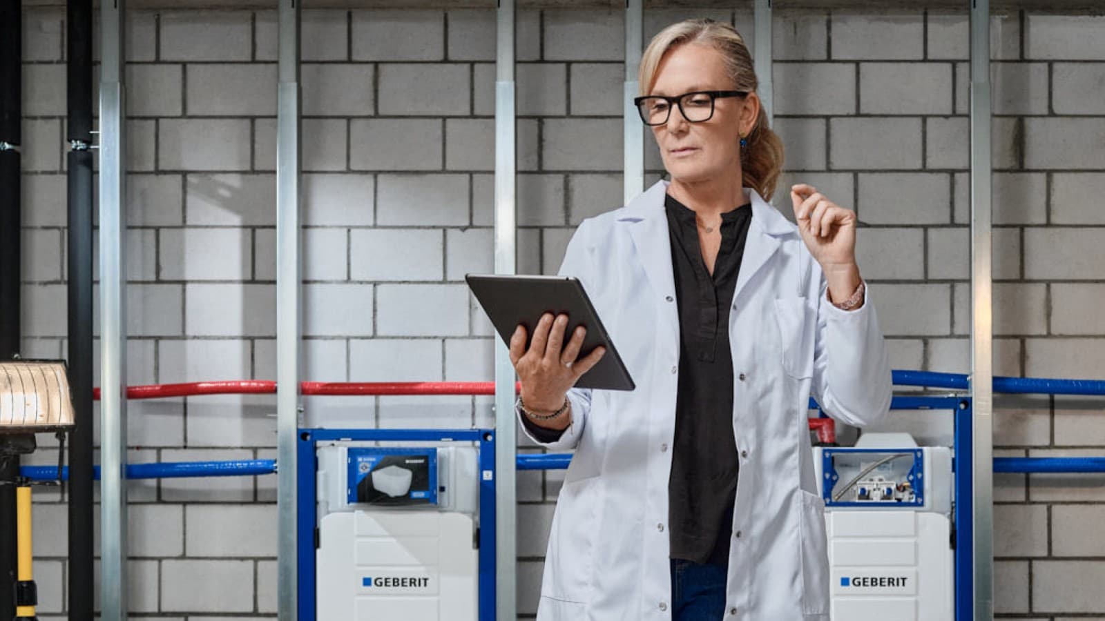 Uno specialista Geberit in camice bianco controlla un'installazione utilizzando un tablet Uno specialista Geberit in camice bianco controlla un'installazione utilizzando un tablet