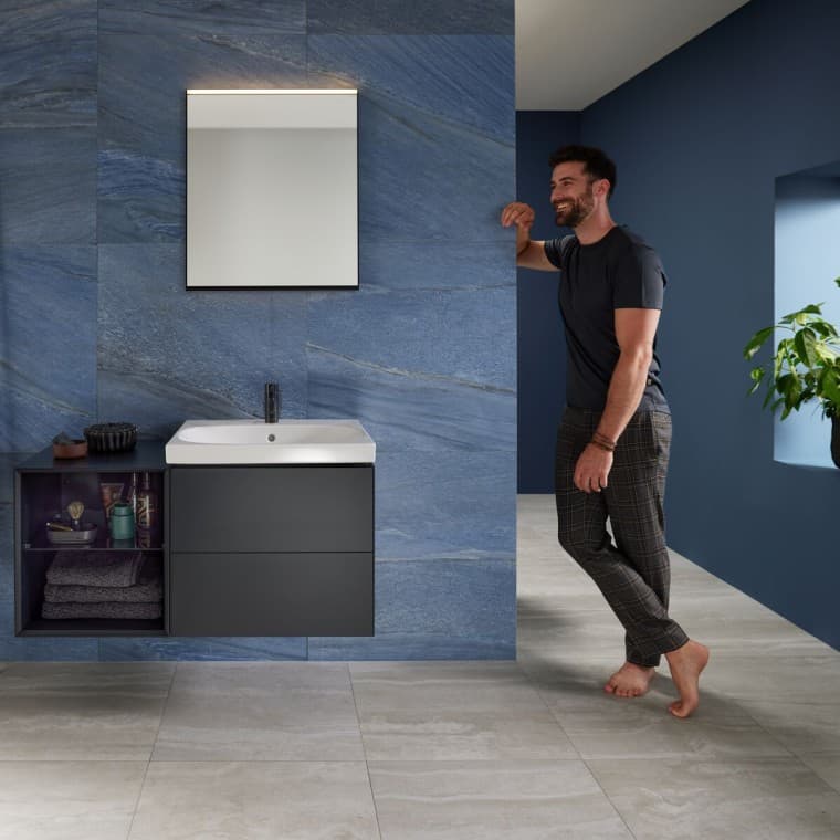 Uomo appoggiato alla parete in un bagno blu con lavabo Geberit Mix & Match Uomo appoggiato alla parete in un bagno blu con lavabo Geberit Mix & Match